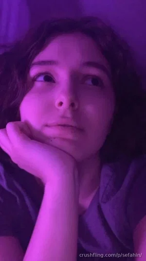Woman with dark curly hair resting her chin on her hand in a dimly lit room with purple lighting.