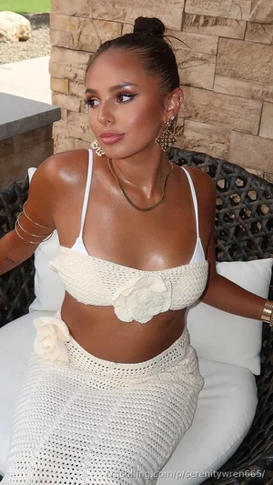 Woman in white crocheted top and skirt sitting on outdoor patio chair.