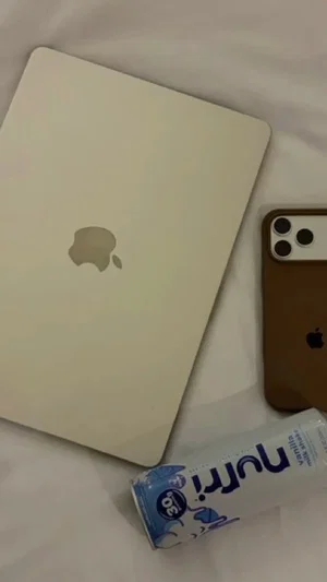 White bed with closed MacBook, iPhone, and Nutri-Go drink can.