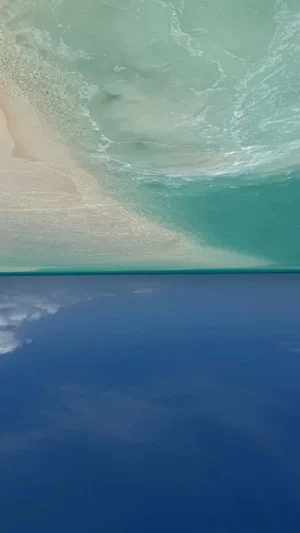Aerial view of turquoise ocean waves meeting sandy beach under blue sky.
