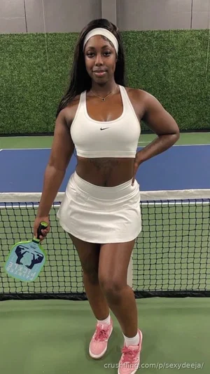 Woman in white sports bra and skirt holding paddle on indoor court.