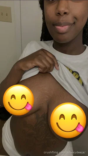 Woman with dark skin and braided hair lifting white t-shirt to expose chest, tattoos visible,