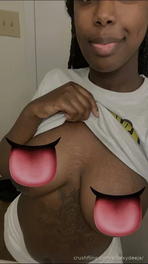 Woman with dark skin and braided hair lifts white t-shirt to expose chest, tattoos visible on