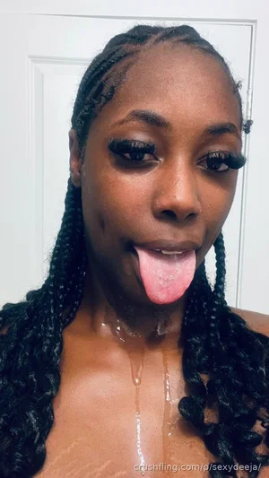 Woman with braided hair, bare shoulders, tongue out, liquid dripping down chest, indoor setting.