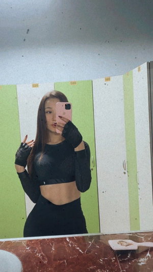 Slim Asian woman in black mesh top and leggings in locker room mirror selfie.