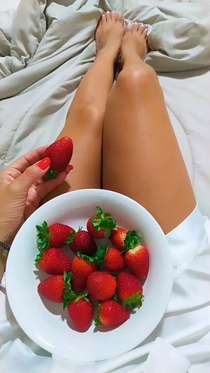 Woman with fit legs on bed holding strawberries.