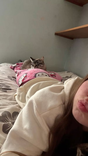 Woman in white hoodie on bed with cat in bedroom.