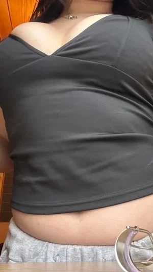 Woman in black top and gray bottoms, showing midriff, indoor setting.