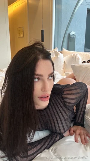 Woman with long dark hair in sheer striped top lying on bed in bedroom.