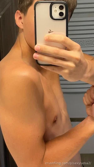 Shirtless man with toned physique taking mirror selfie indoors.