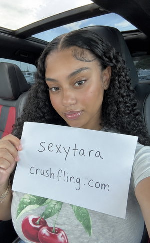 Woman with curly hair holding sign in car interior.