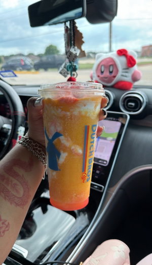 Hand holding orange drink in car with dragon tattoo and Kirby plush.