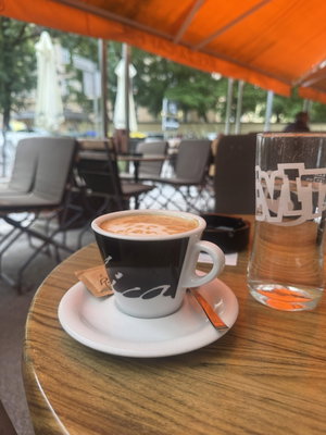 Coffee cup and glass on wooden table under orange canopy, outdoor seating area.