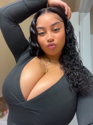 Woman with curly black hair in a black top posing indoors, hand in hair.