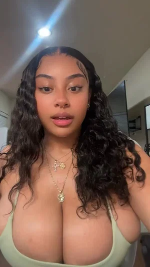 Buxom woman with curly black hair in green tube top indoors.
