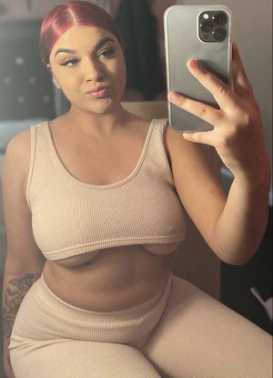Woman with red hair in beige outfit taking mirror selfie indoors.