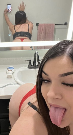 Woman in red lingerie taking mirror selfie in bathroom.