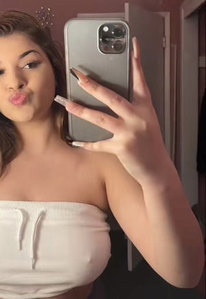 Woman with brown hair taking mirror selfie in white strapless top.