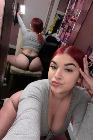 Red-haired woman in gray top taking mirror selfie indoors.