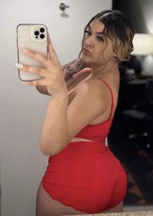 Woman in red lingerie taking mirror selfie, tattooed arm, indoor setting.