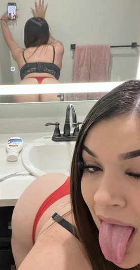 Woman in red underwear and black lace top taking mirror selfie in bathroom.