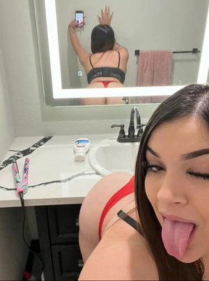 Woman in red lingerie taking mirror selfie in bathroom.