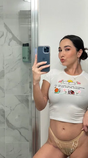 Woman in white crop top and beige lace underwear posing in bathroom mirror selfie.
