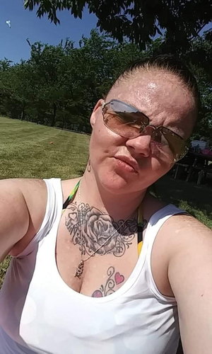 Woman with tattoos wearing white tank top outdoors.