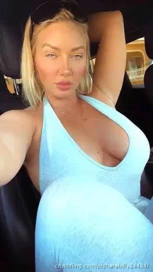Blonde woman in light blue halter dress sitting in car, taking selfie.