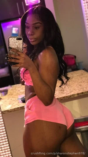 Woman with long dark hair in pink lingerie taking mirror selfie in kitchen.