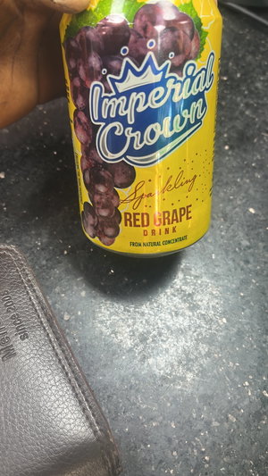 Hand holding yellow grape drink can next to wallet.