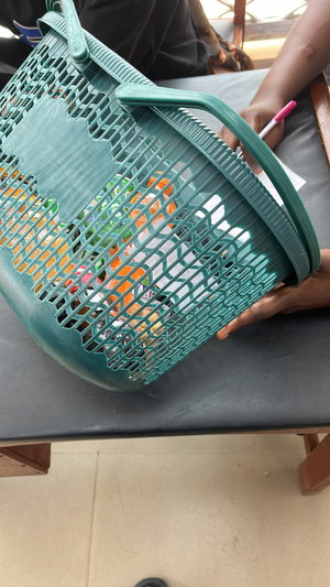 Dark-skinned hands in black top hold green basket on table.