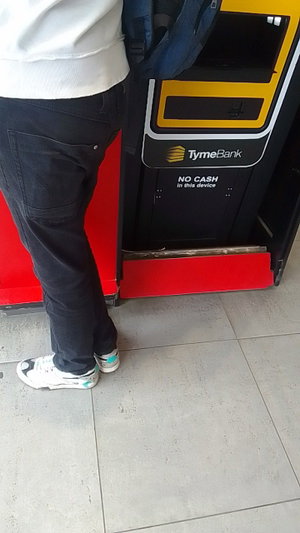 Slim man in white hoodie and jeans at ATM.