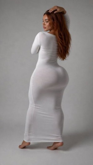 Woman with long brown hair in white dress posing in studio.