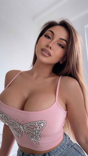 Woman with long brown hair in pink top and jeans indoors.
