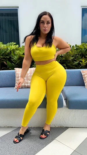 Woman in yellow crop top and leggings posing outdoors near blue sofa.