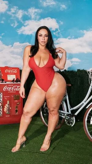 Woman in red one-piece swimsuit posing outdoors near vintage Coca-Cola machine and bike.