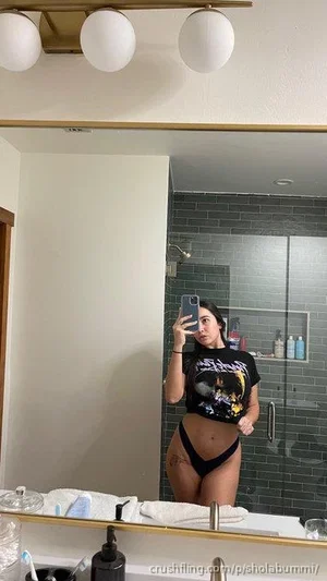 Woman in black crop top and thong taking mirror selfie in bathroom.