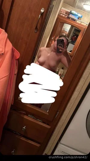 Woman with bare chest taking mirror selfie in bathroom, wearing no top, partial body visible.