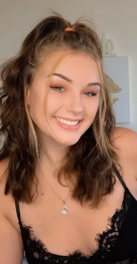 Smiling woman with brown hair in black lace top indoors.