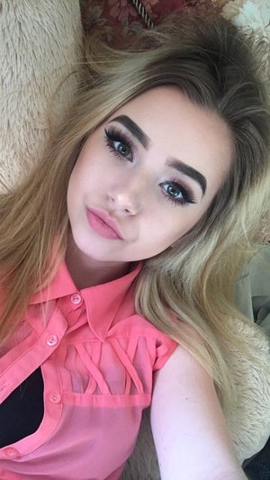 Woman with blonde hair in pink sleeveless shirt lying on fluffy surface.