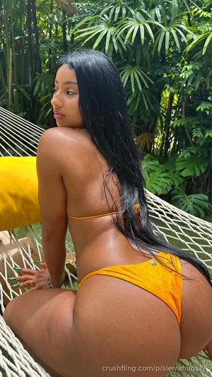 Woman with long black hair in orange bikini sitting in hammock outdoors.
