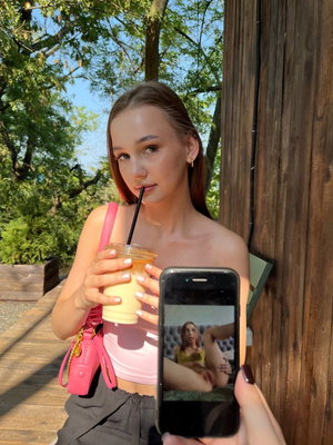 Woman in pink top holding drink outdoors.