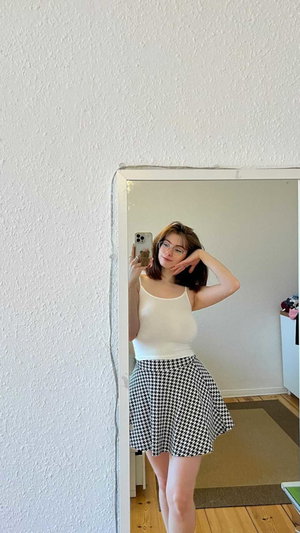 Woman with glasses taking mirror selfie in white top and skirt.