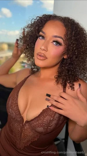 Woman with curly hair in brown lace top posing outdoors on balcony.