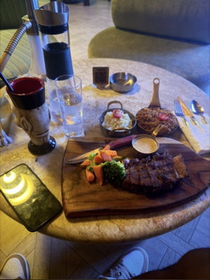 Restaurant table with steak, sides, hookah and drinks.