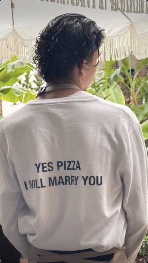 Curly-haired person in white sweatshirt seen from behind outdoors.
