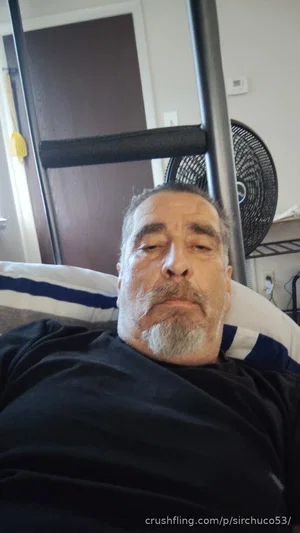 Man with gray beard wearing black shirt, lying on striped pillow indoors.