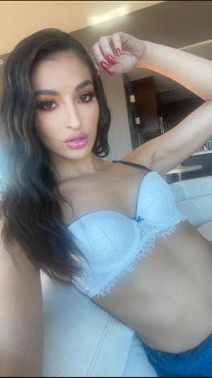 Woman with long dark hair wearing light blue bra indoors.