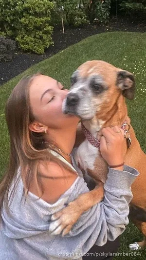 Woman in gray off-shoulder top hugging dog in grassy outdoor setting.